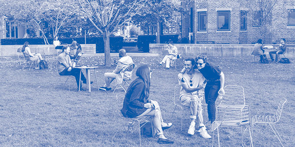 GSD students and faculty sit together at assorted cafe-style tables in on a grassy lawn in a photo taken fall 2021. 