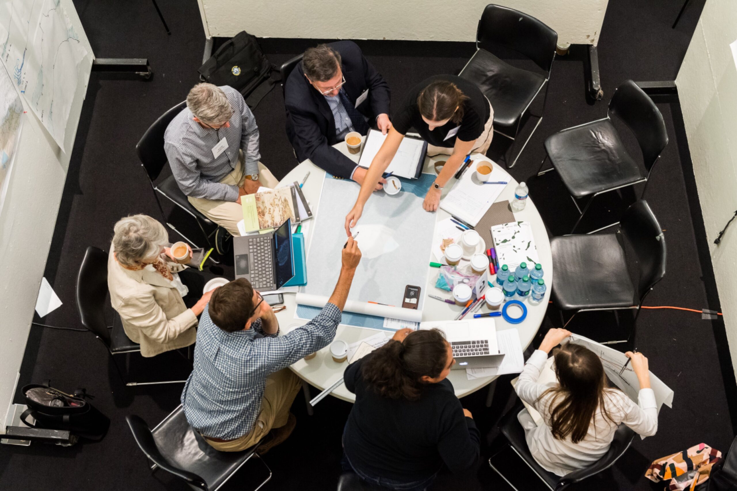 Seven people sitting at a round table brainstorming and drafting a plan.