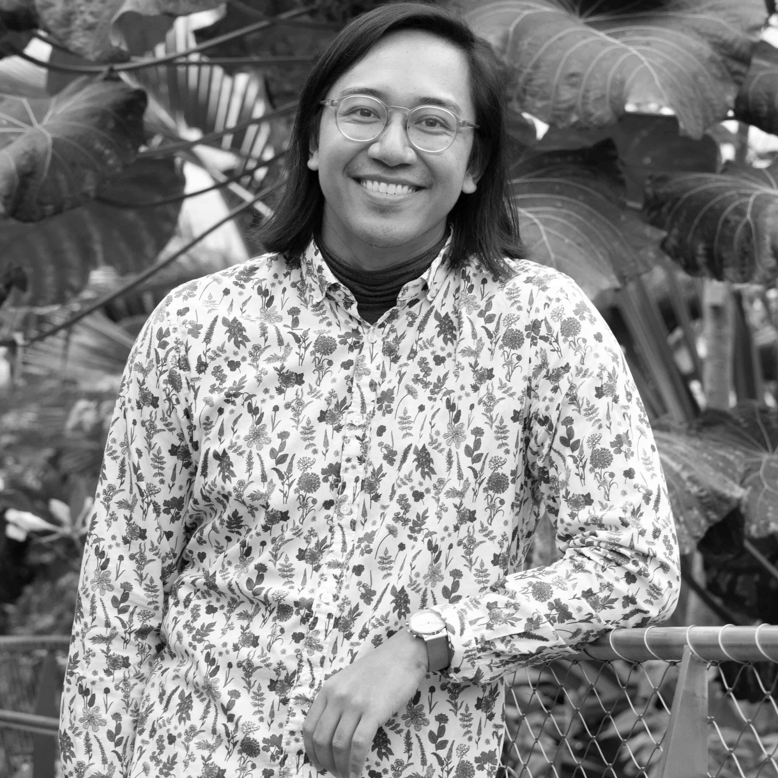 Black and white square headshot of Estello in a white floral button up with plants in the background