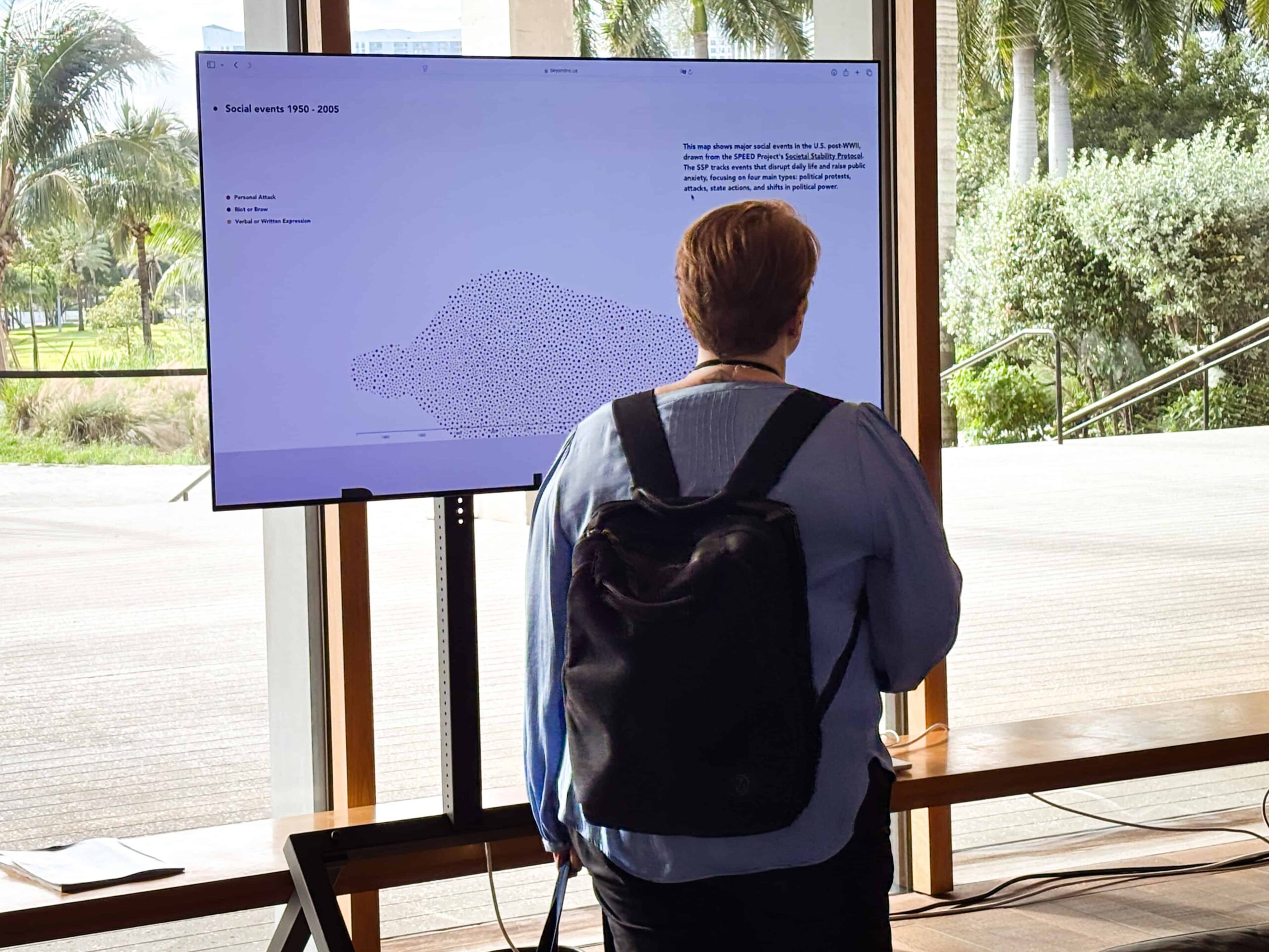 A person with a backpack standing in front of a white screen with data on it.