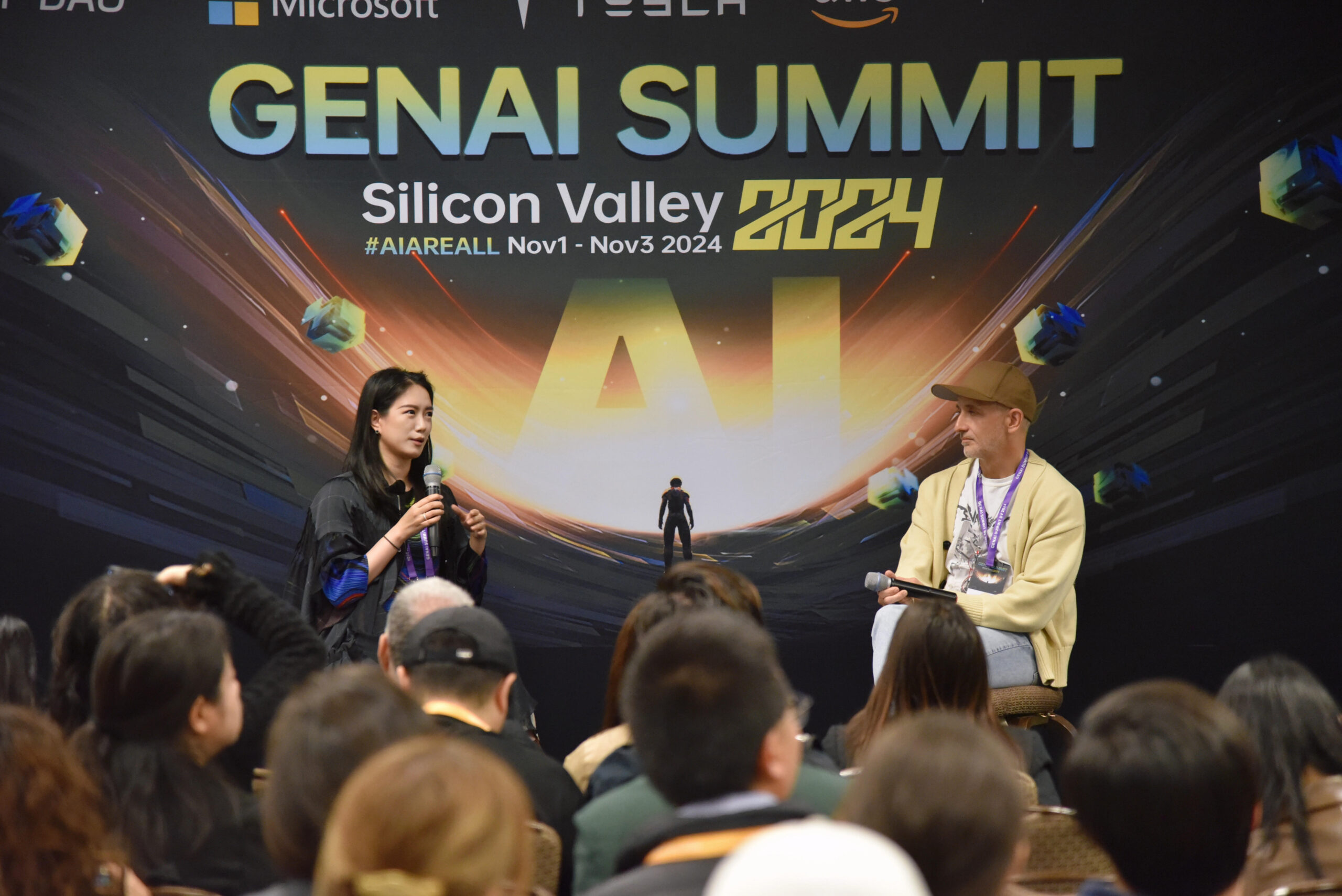 Yiqi Zhao on a panel with Charles Migos. Both speakers are facing each other with a backdrop that reads "GenAI Summit". Yiqi holds a microphone in her hands.